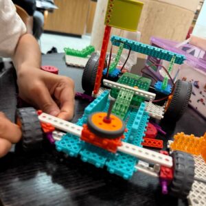 Kids assembling a functional car robot with sensors in an intermediate robotics workshop, developing problem-solving and engineering skills for ages 6-12.